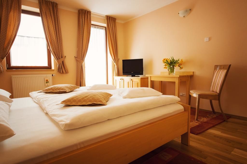 A hotel room with a bed, a TV, a desk with a vase of flowers, and a chair.