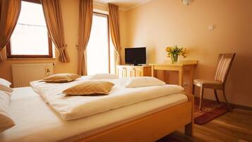 A hotel room with a bed, a TV, a desk with a vase of flowers, and a chair.