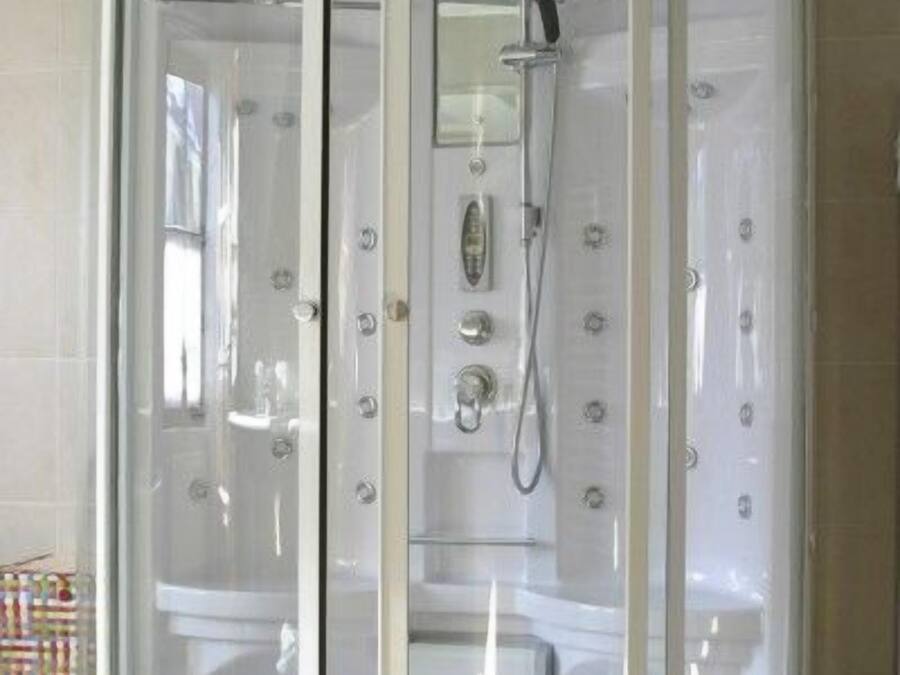 A modern, enclosed shower area with a glass door, built-in controls, and a handheld showerhead.