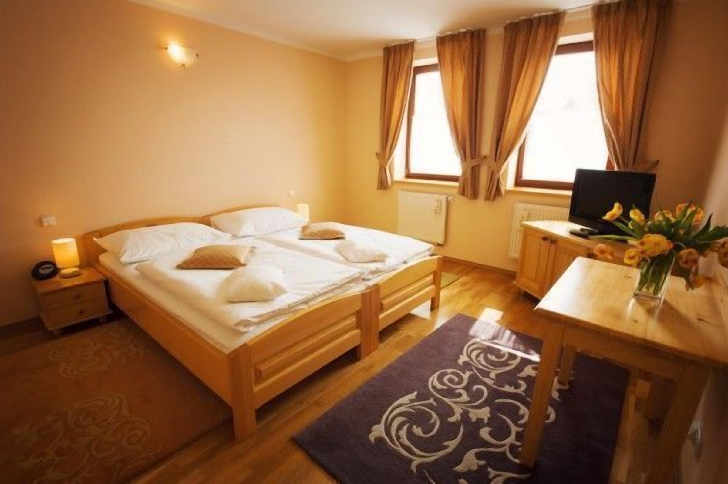 Ein Hotelzimmer mit einem hölzernen Bett, einem Schreibtisch mit einem Laptop, einem Fernseher und einer Vase mit Blumen.