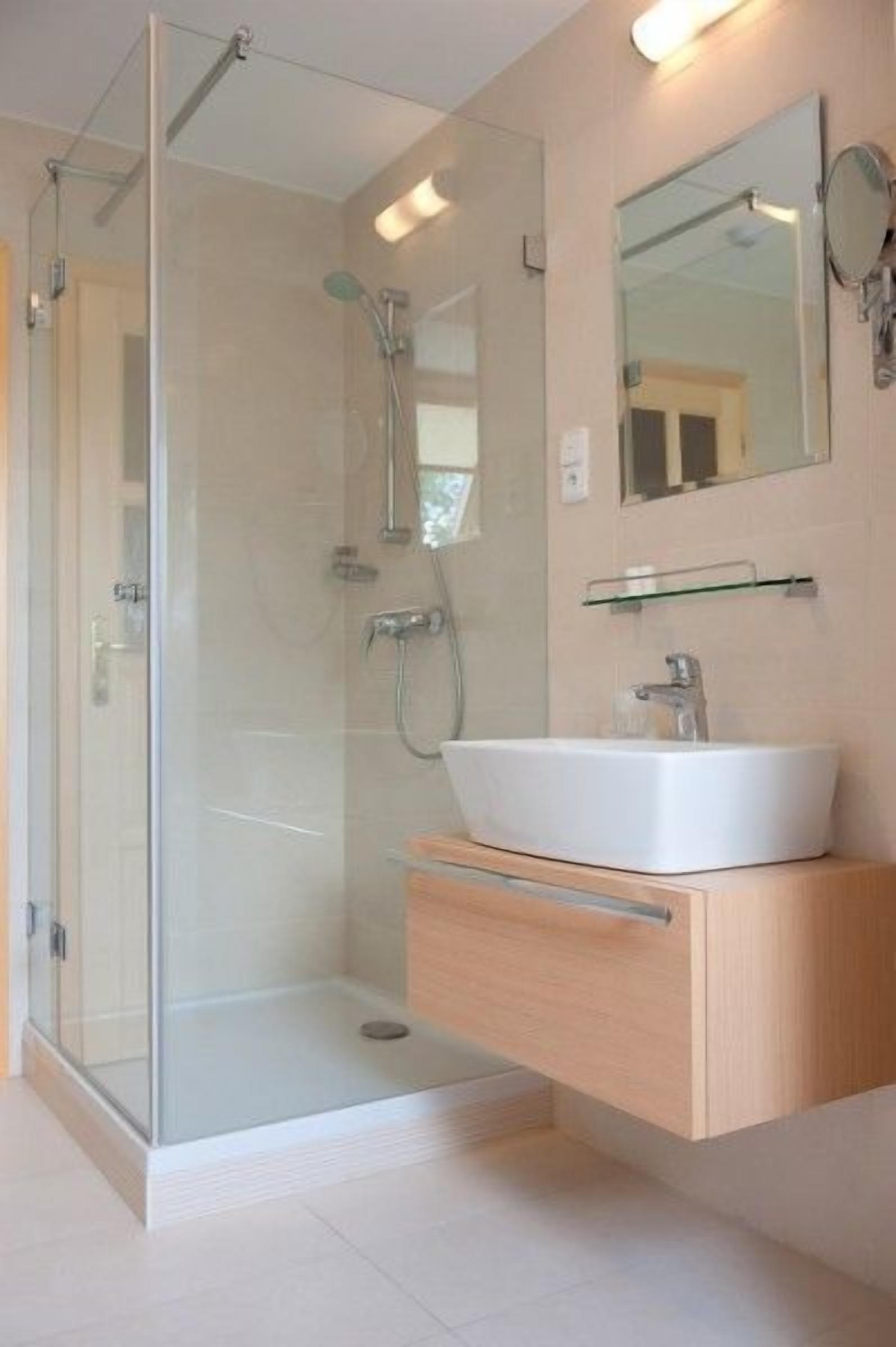 A modern bathroom with a glass-enclosed shower, a white sink, and a mirror above it.