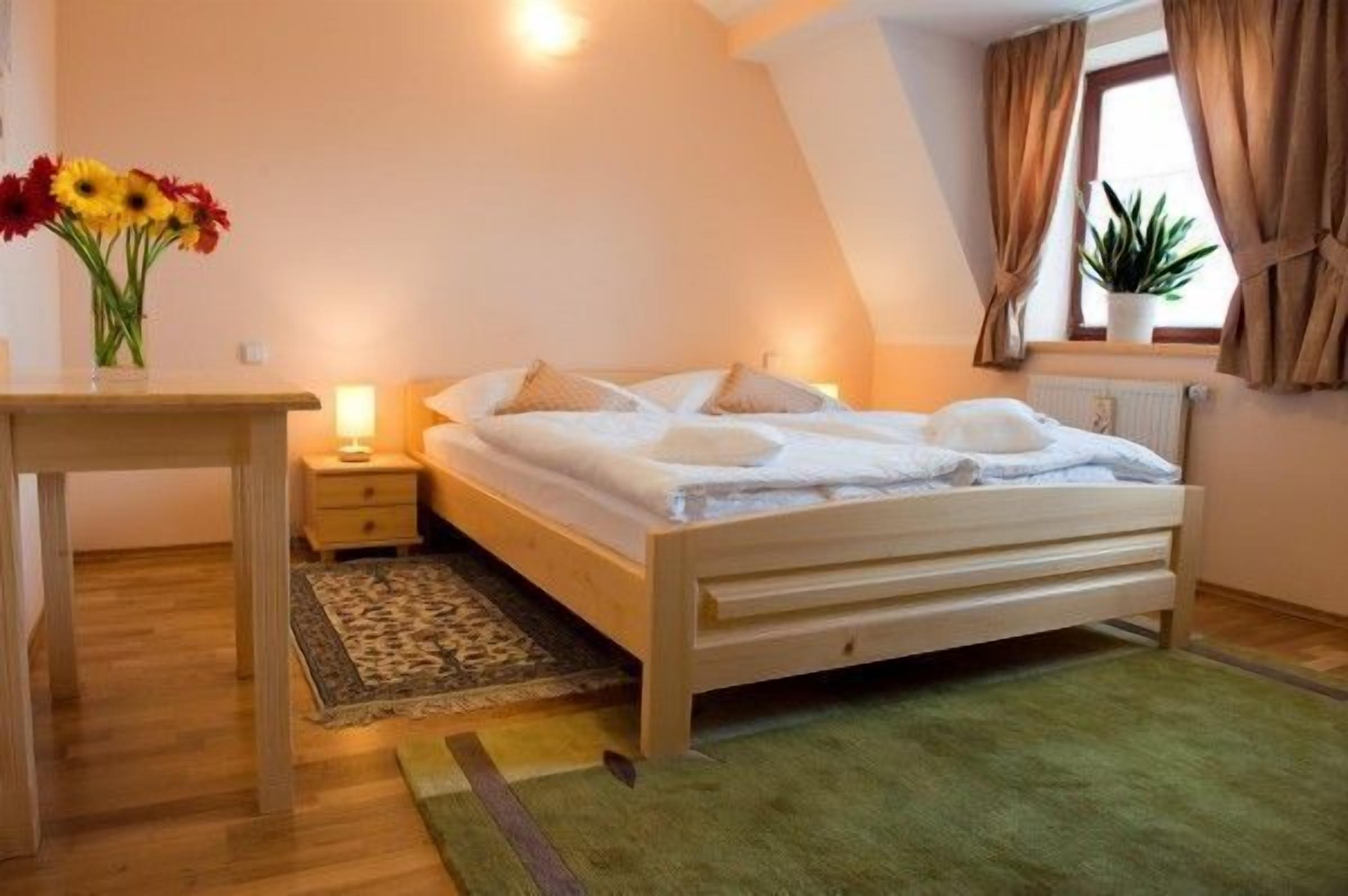 A bedroom with a wooden bed, bedside table, lamp, and a potted plant by the window.