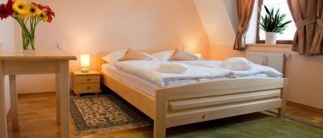 A bedroom with a wooden bed, bedside table, lamp, and a potted plant by the window.