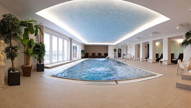 An indoor swimming pool with a hot tub, surrounded by seating areas and potted plants. - Hotel Karpatsky Dvor (Lozorno)