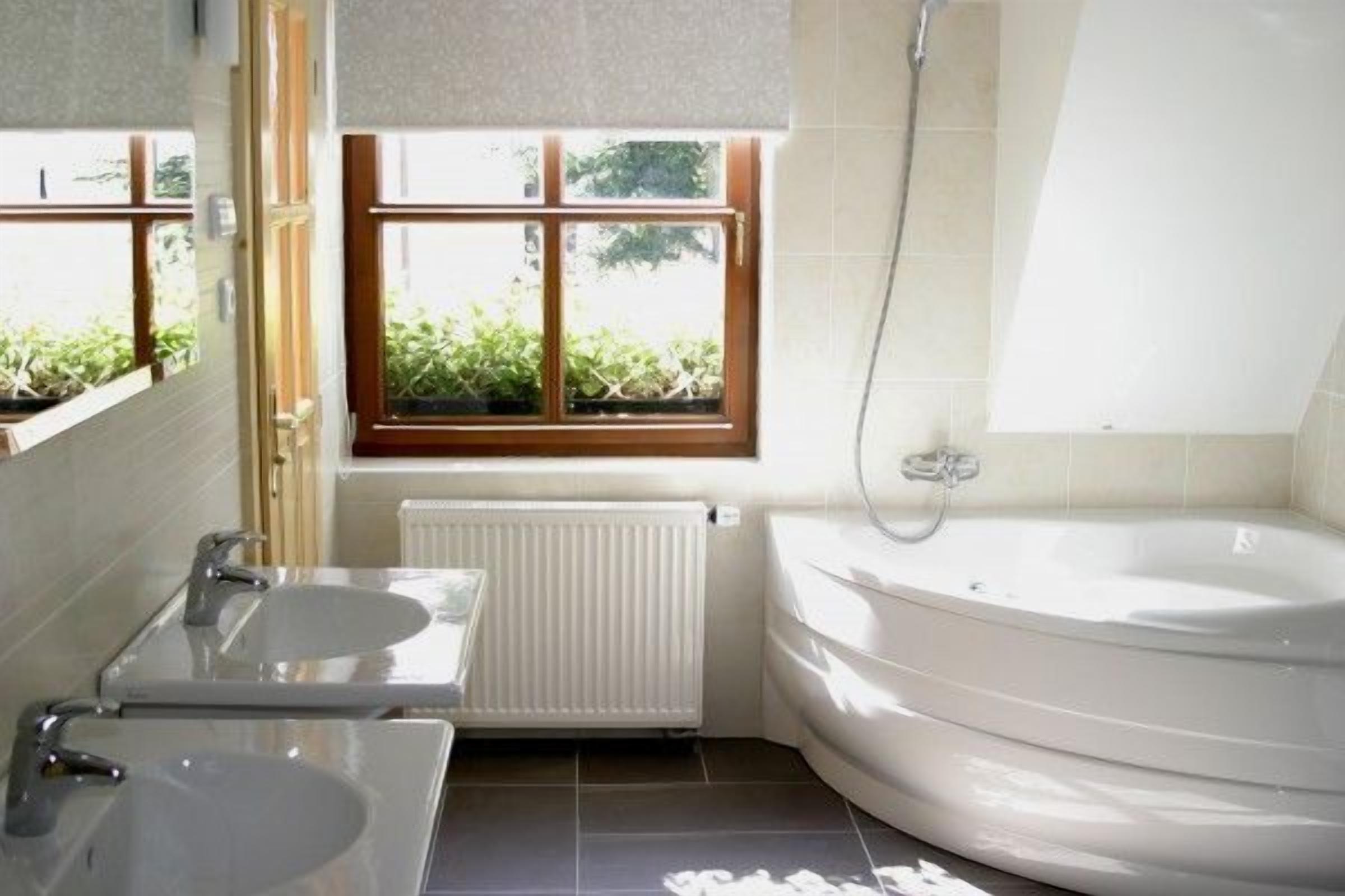 A bathroom with two sinks, a bathtub, a window with a view of greenery, and a radiator.