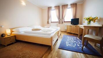 Un dormitorio con cama, mesita de noche, lámpara, televisor, escritorio de madera, silla y ventana con cortinas.