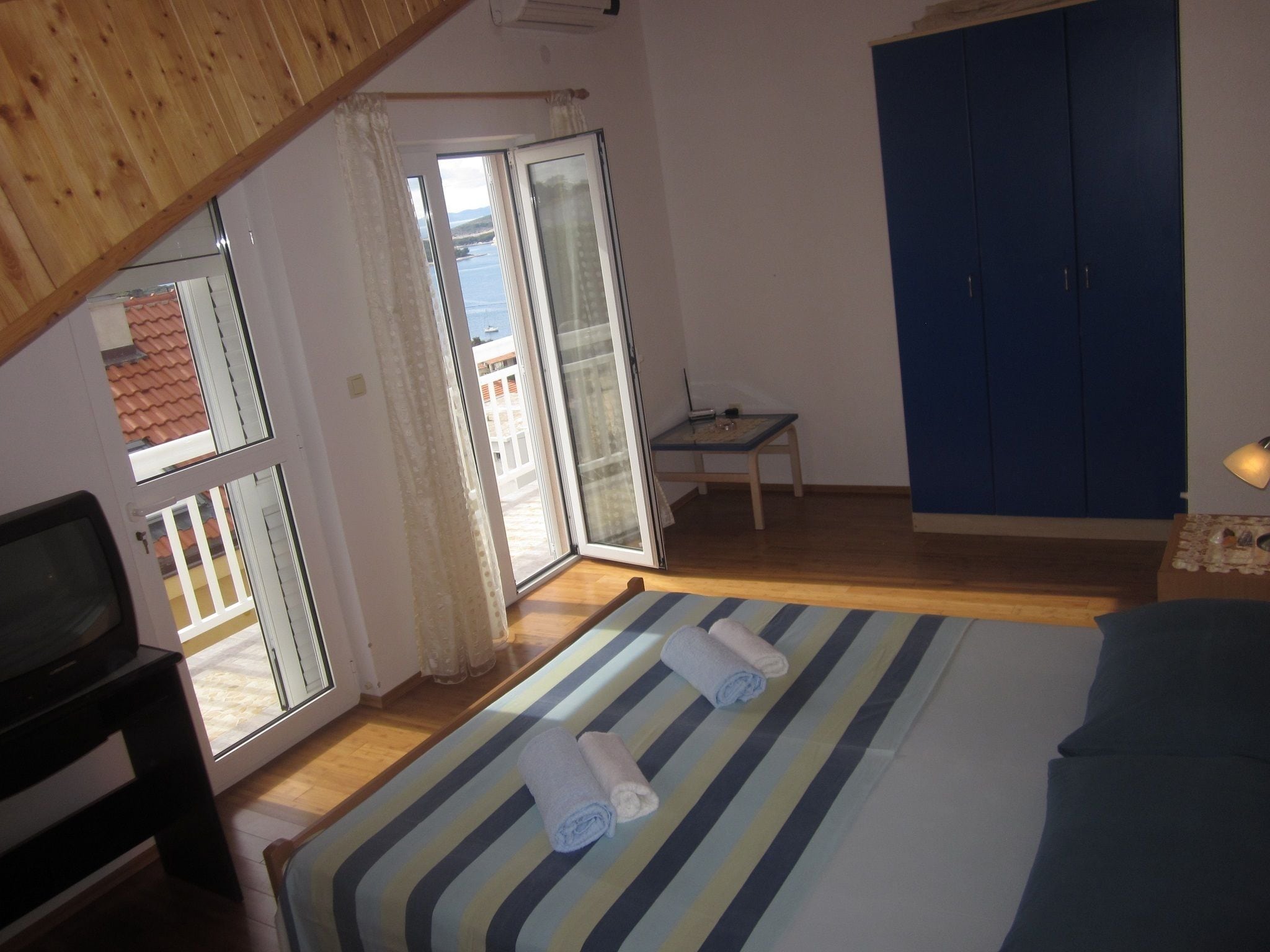 A bedroom with a bed, a desk, a chair, a TV, and a view of the outside.