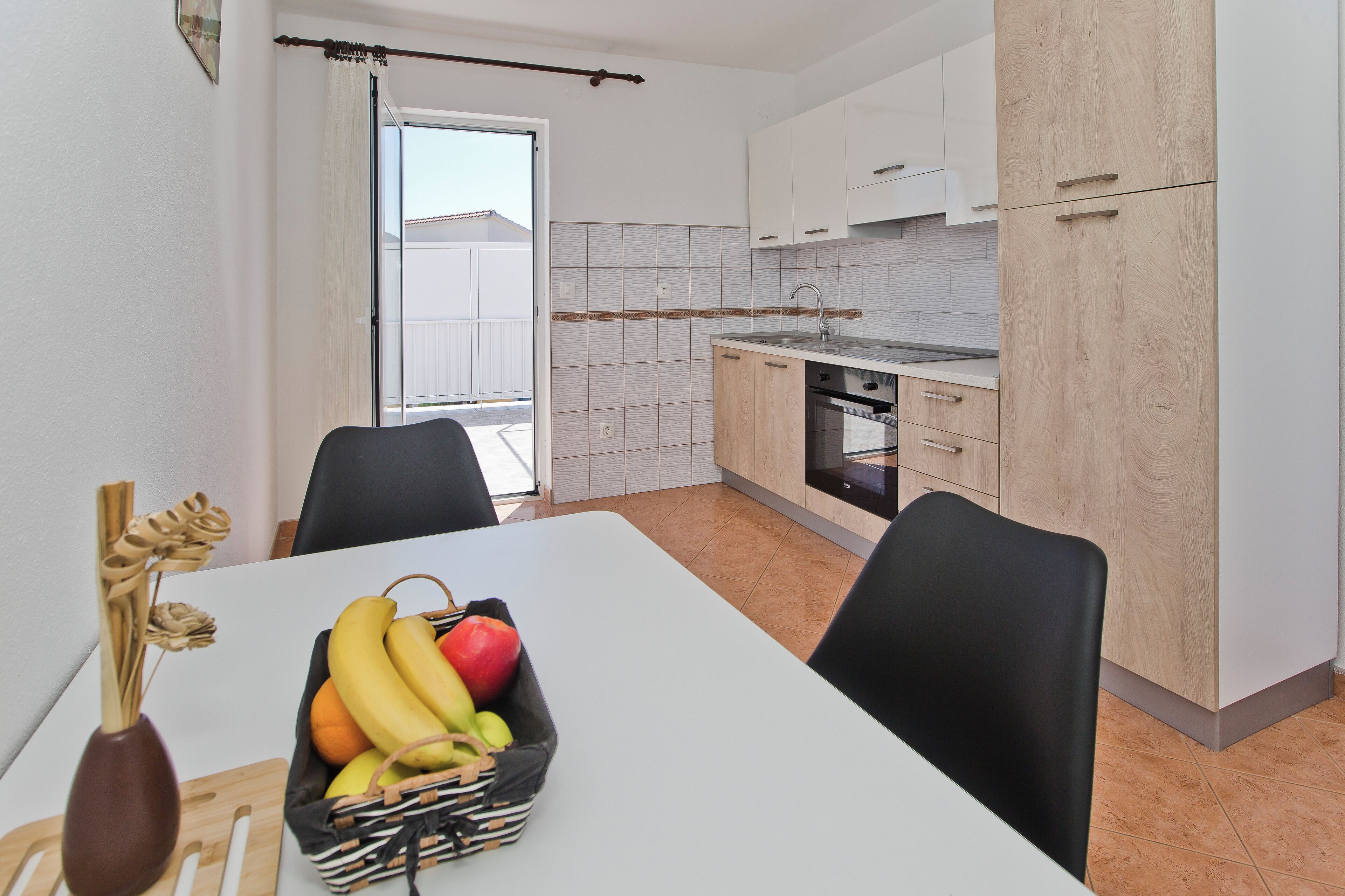 A modern kitchen with white cabinets, a dining table with chairs, and a fruit basket on the table.