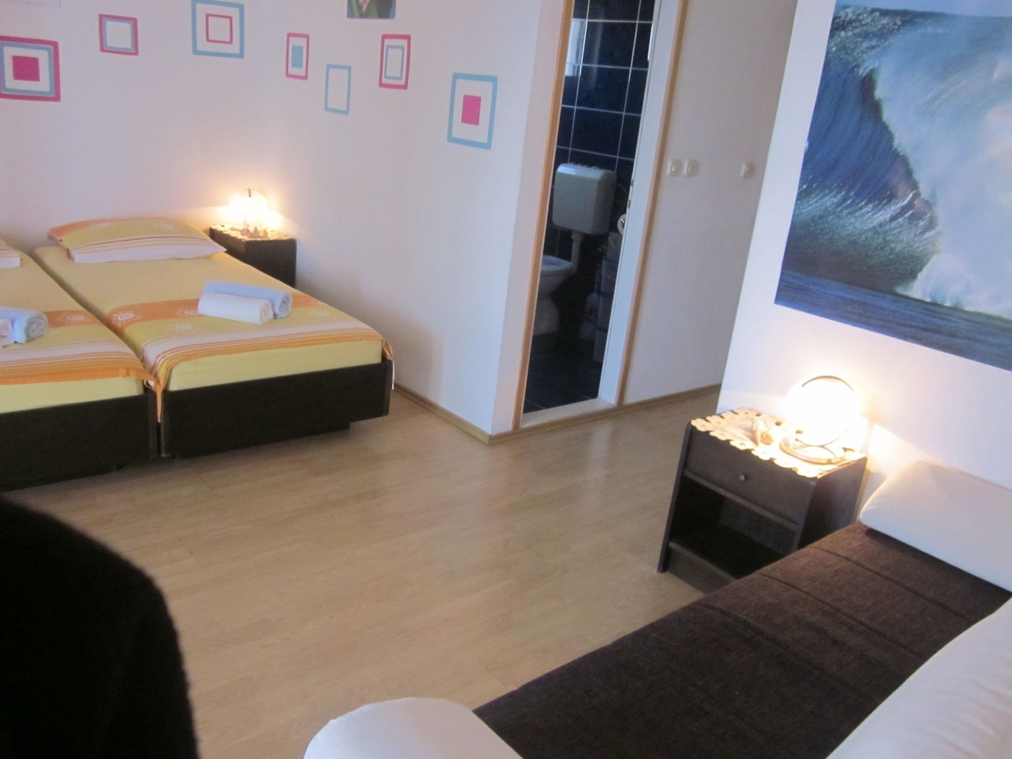 Ein Hotelzimmer mit zwei Betten, einem kleinen Tisch mit einer Lampe, einem Wellenbild und einer Schiebetür zu einem Badezimmer.