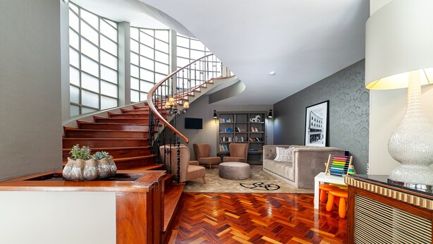 A spacious living area with a wooden herringbone floor, a curved staircase, and a large window providing natural light. - Hotel Porto Mar (Matosinhos)
