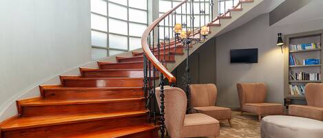 A wooden staircase with a curved design, a chandelier, and a bookshelf with books.