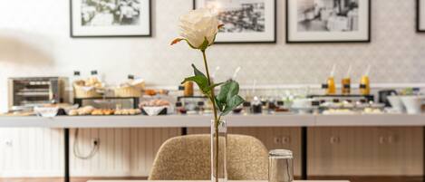A dining table with a white rose in a clear vase, a water pitcher, and a teapot. There are framed pictures on the wall behind the table.