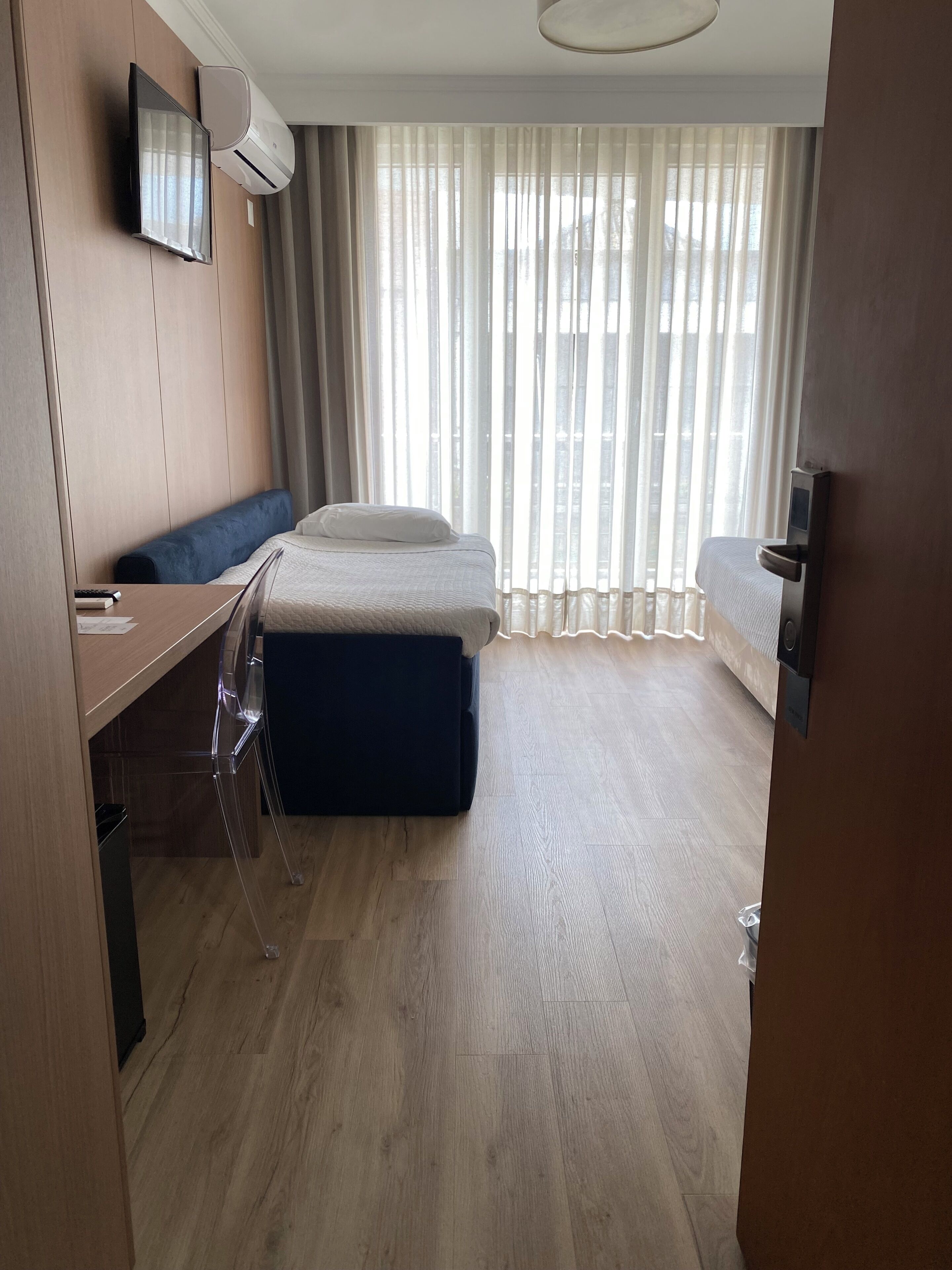 A hotel room with a bed, a desk, a chair, a TV, and a window with curtains.