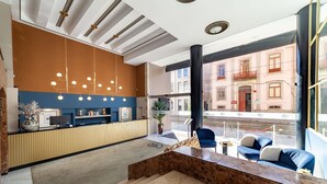 A modern hotel lobby with a reception desk, seating area, and large windows offering views of the street. - Hotel Porto Mar (Matosinhos)