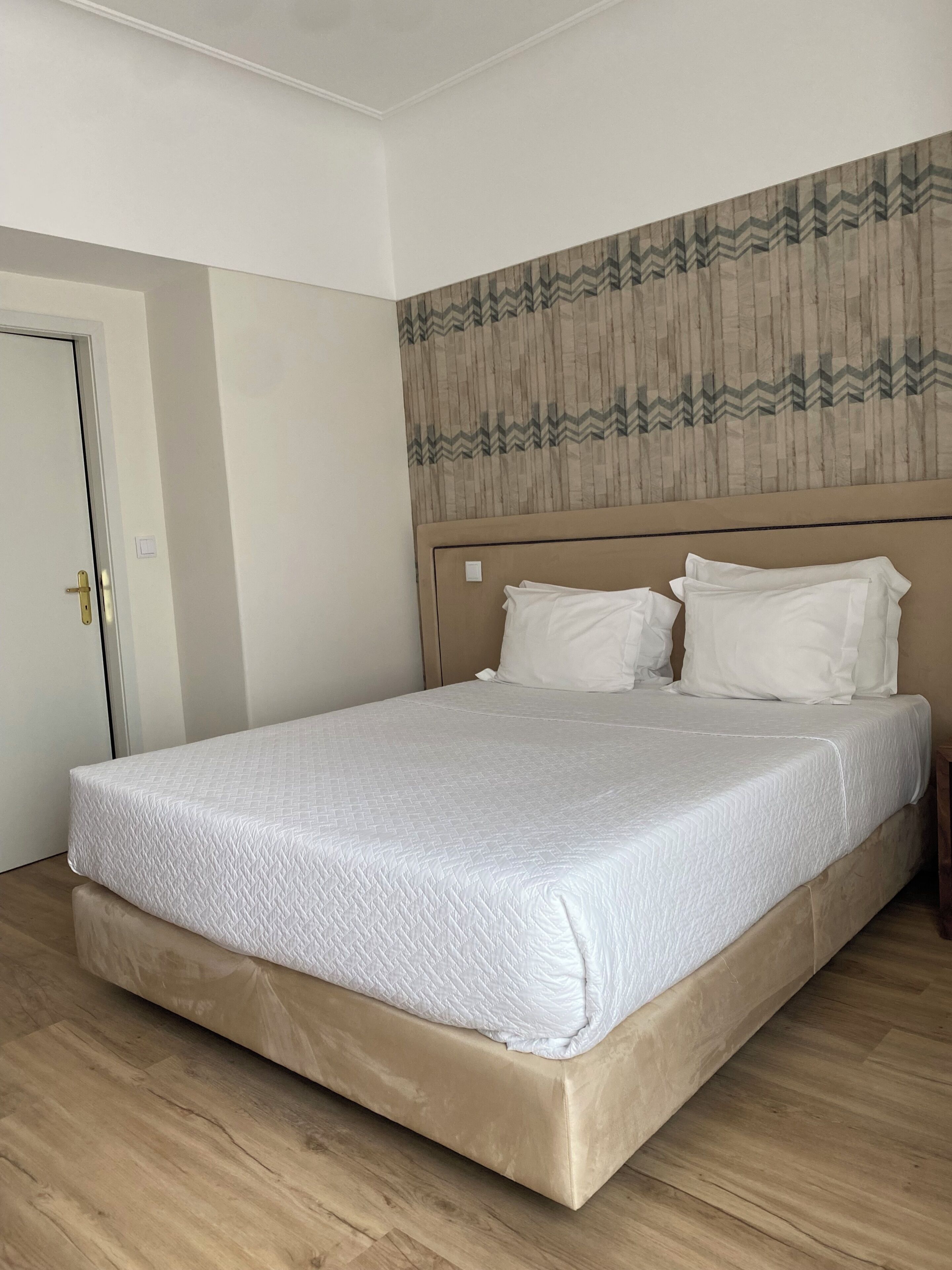 Een bed met een geborduurde matras, een houten hoofdbord en een behang met een patroon aan de muur.