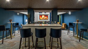 A bar area with a central island, bar stools, and a television screen displaying a fire. - Hotel Porto Mar (Matosinhos)