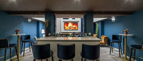 A bar area with a central island, bar stools, and a television screen displaying a fire.