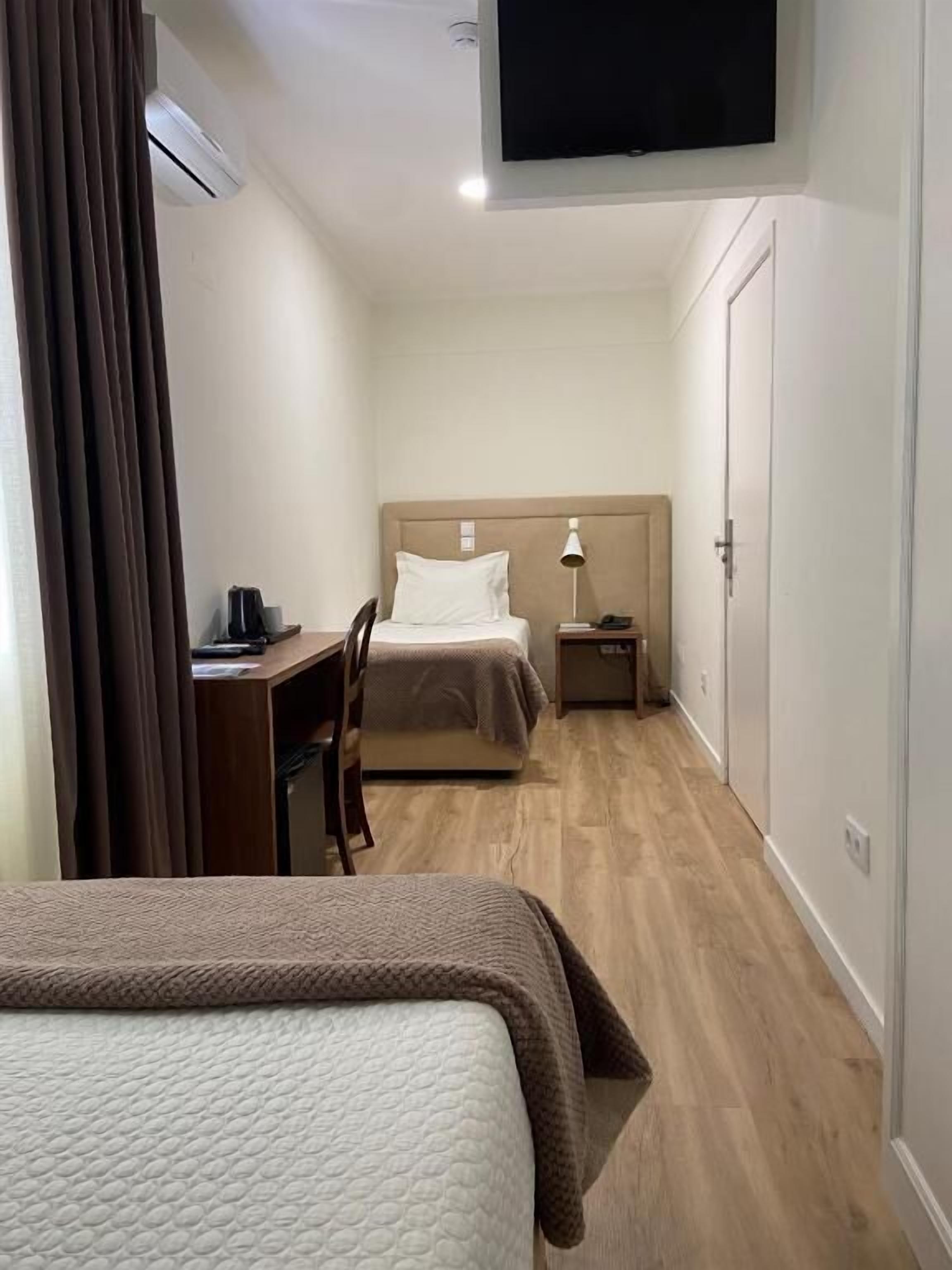 Une chambre d’hôtel avec deux lits, un bureau, une chaise, une table de chevet, une lampe et un téléviseur fixé au mur.