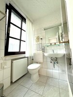 Uma casa de banho com sanita, lavatório, espelho e janela com cortinas.