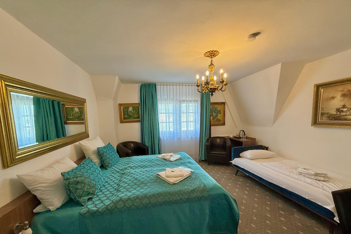 Habitación de hotel con dos camas individuales, un escritorio, una silla, una araña y obras de arte en las paredes.