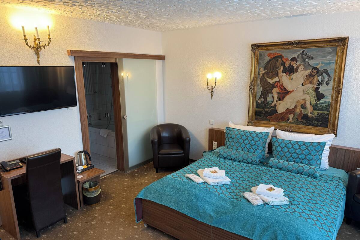 Habitación de hotel con cama, escritorio, silla, televisor, un cuadro y zona de ducha.