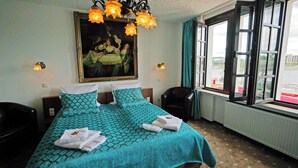 A hotel room with a bed, a chair, a painting, and a window with a view. - Löwenbräu Köln Hotel & Restaurant (Cologne)