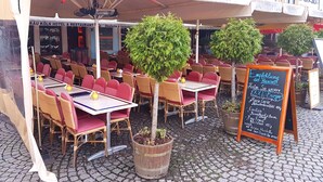 An outdoor seating area of a restaurant with tables and chairs, potted plants, and a chalkboard menu board. - Löwenbräu Köln Hotel & Restaurant (Cologne)