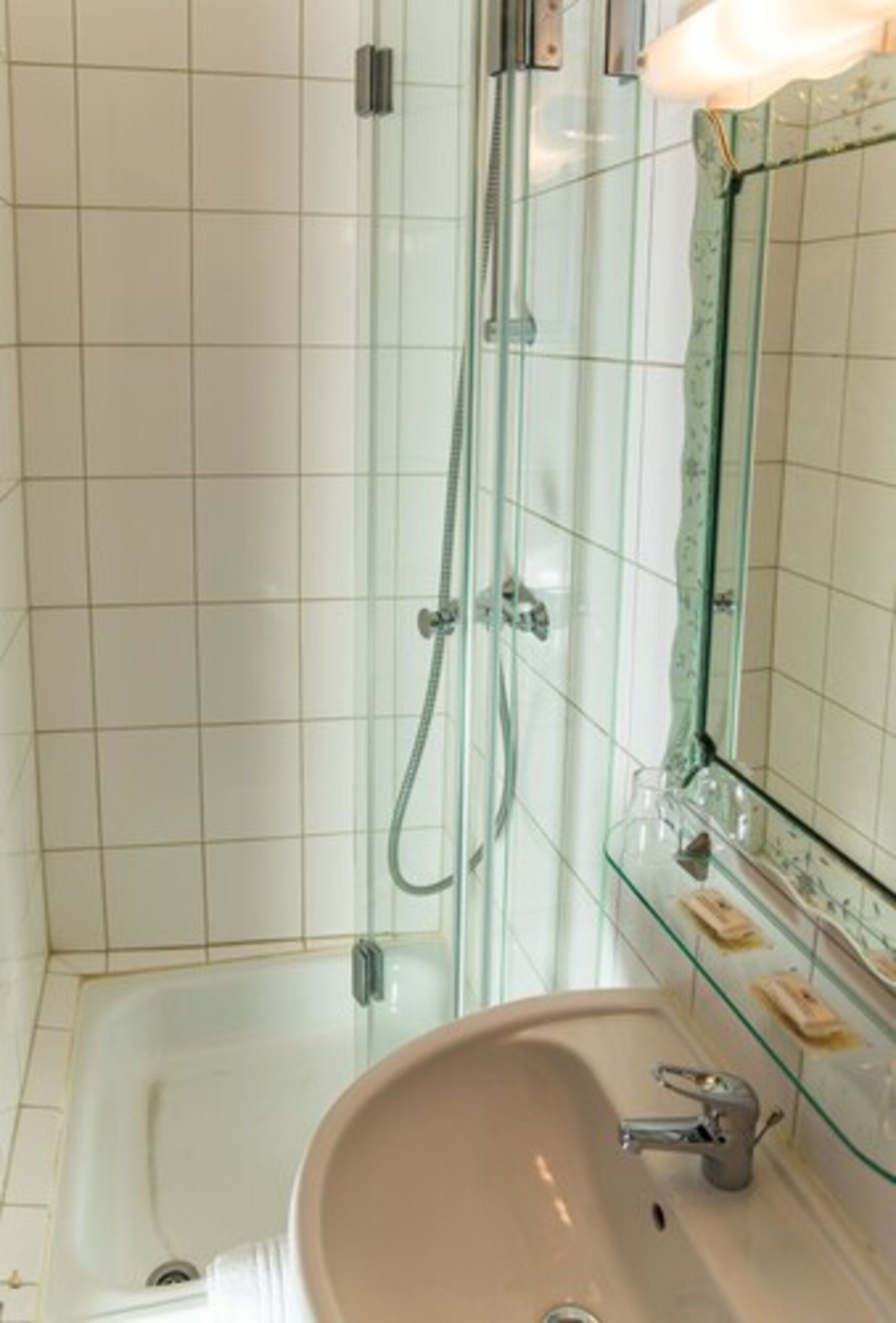 Un baño con ducha de mampara de vidrio, un lavamanos con espejo y un estante de vidrio con artículos de tocador.