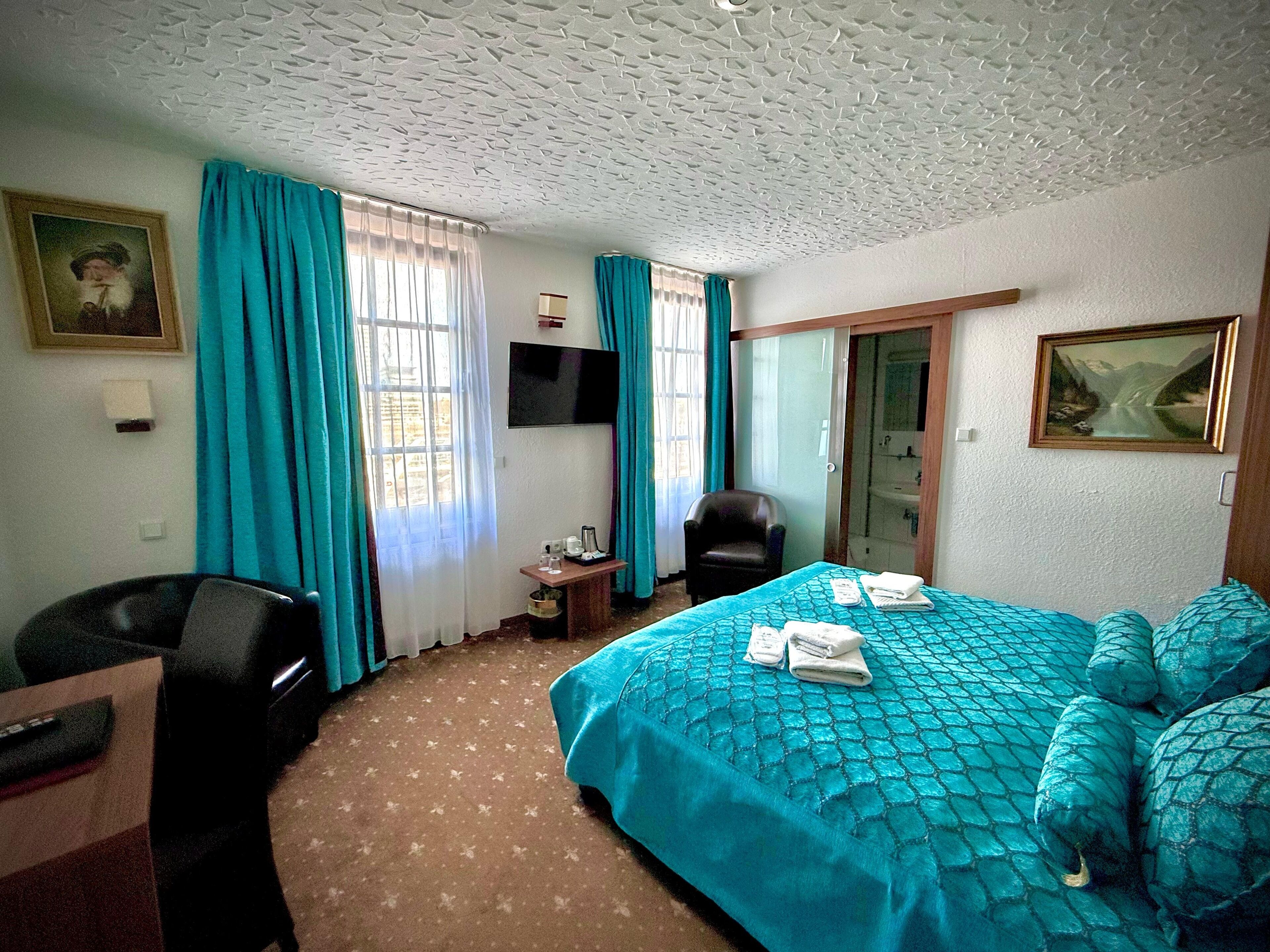 A hotel room with a bed, a desk, a chair, a television, and a bathroom visible through an open door.