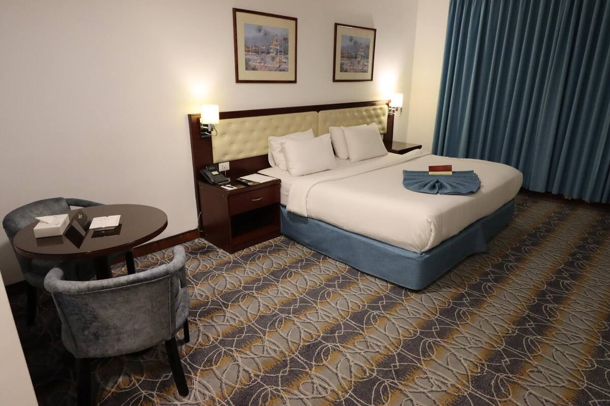 A hotel room with a bed, a desk, a chair, and two framed pictures on the wall.