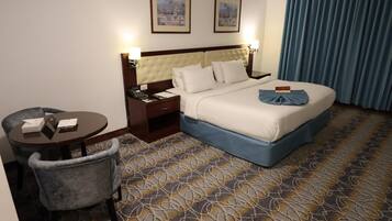 A hotel room with a bed, a desk, a chair, and two framed pictures on the wall.