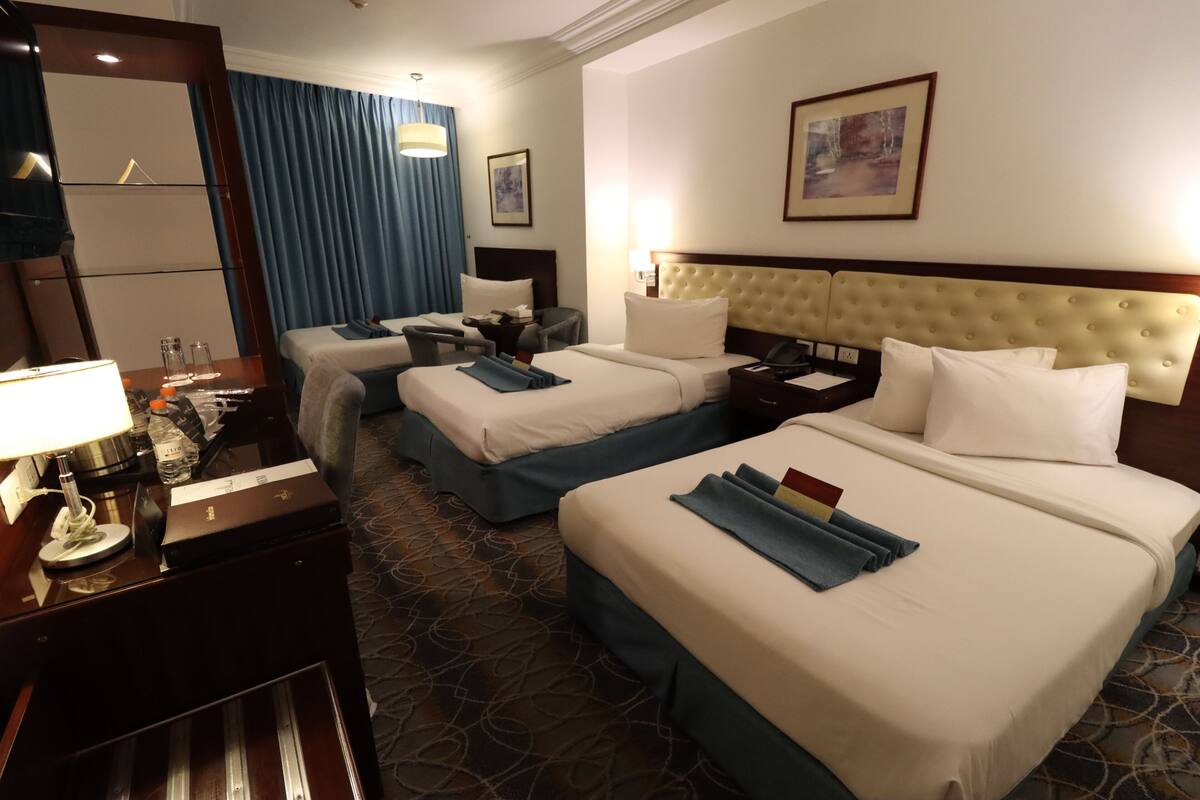 A hotel room with two beds, a desk with a lamp, a nightstand, and a large mirror.