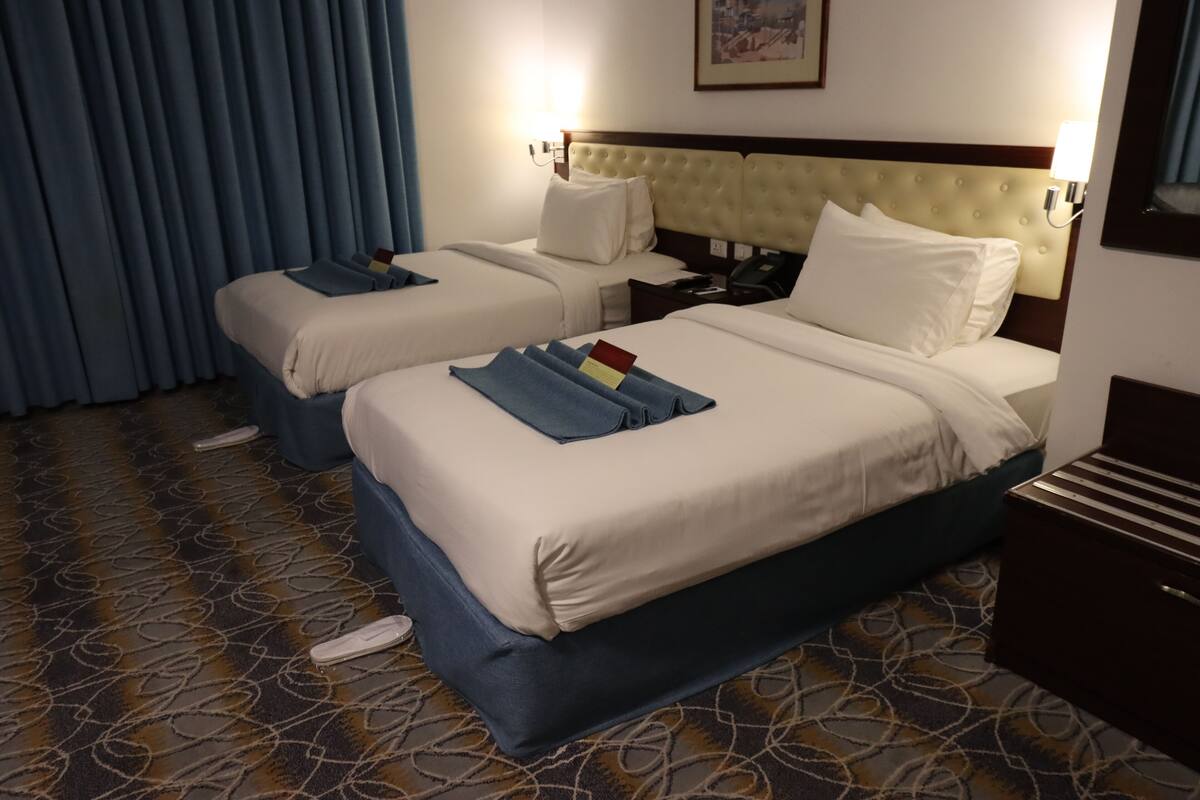 A hotel room with two beds, a headboard, bedside tables, a telephone, and a carpeted floor.