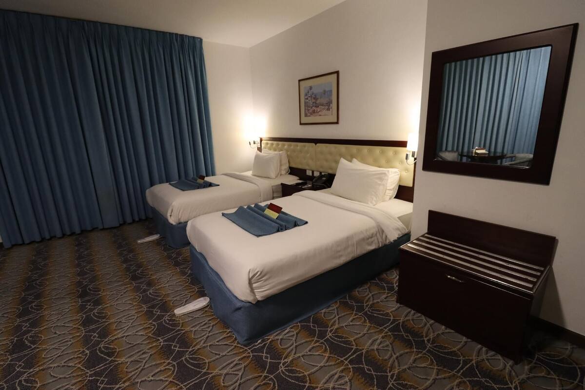 A hotel room with two beds, a headboard, a bedside table, a mirror, and a patterned carpet.