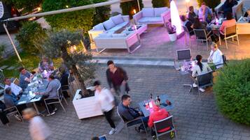An outdoor dining area with multiple tables and chairs, surrounded by greenery and a white sofa.