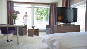 A hotel room with a bed, a TV, a desk with a chair, and a view of the outdoors. - Cityhotel Design & Classic (St. Pölten)