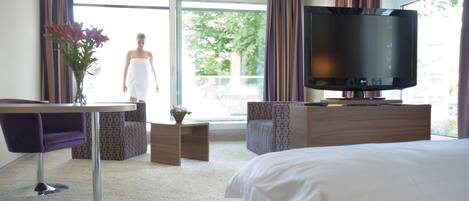 A hotel room with a bed, a TV, a desk with a chair, and a view of the outdoors.