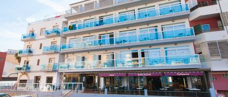 Een hotel met meerdere verdiepingen, balkons, een café en een parkeerplaats.
