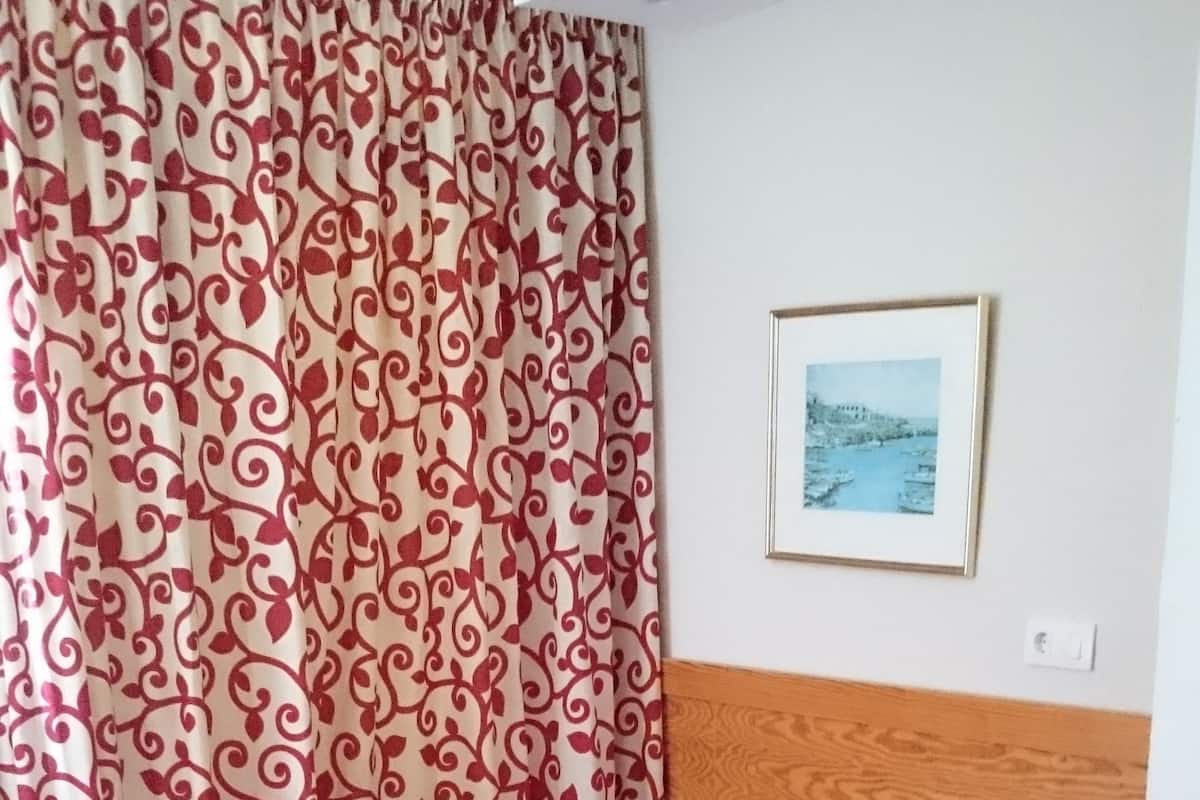 A bedroom with a bed, a nightstand, a wooden headboard, a framed picture on the wall, and a patterned curtain.