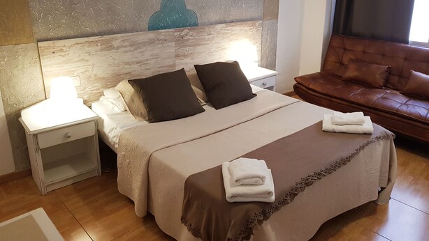 Een hotelkamer met een bed, twee nachtkastjes, een bruine leren bank en een groot abstract schilderij aan de muur.