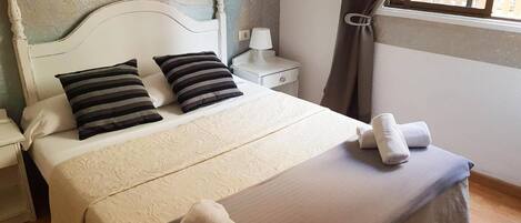 A neatly made bed with pillows, a bedside table with a lamp, and a window with curtains.