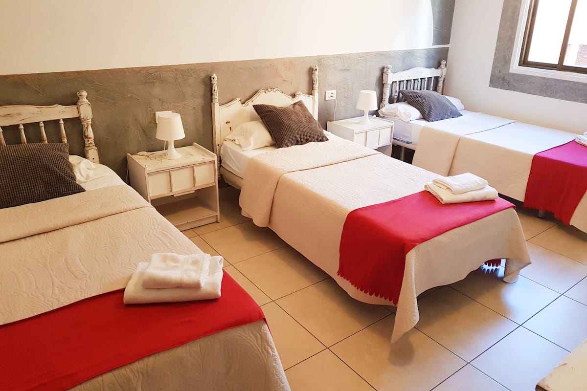 Une chambre d’hôtel avec deux lits simples, un lit double et une petite table avec une lampe.