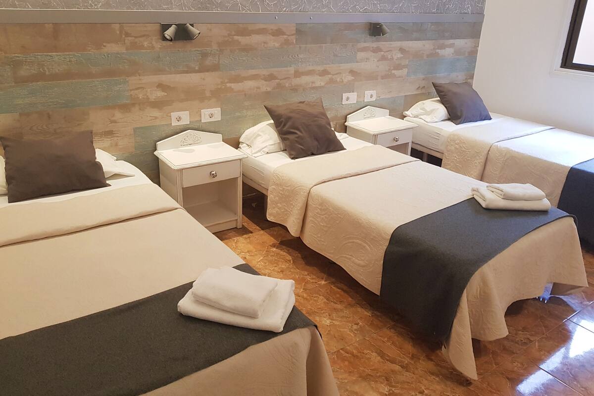 Une chambre d’hôtel avec deux lits, une table de chevet, une petite table et un mur au décor texturé.