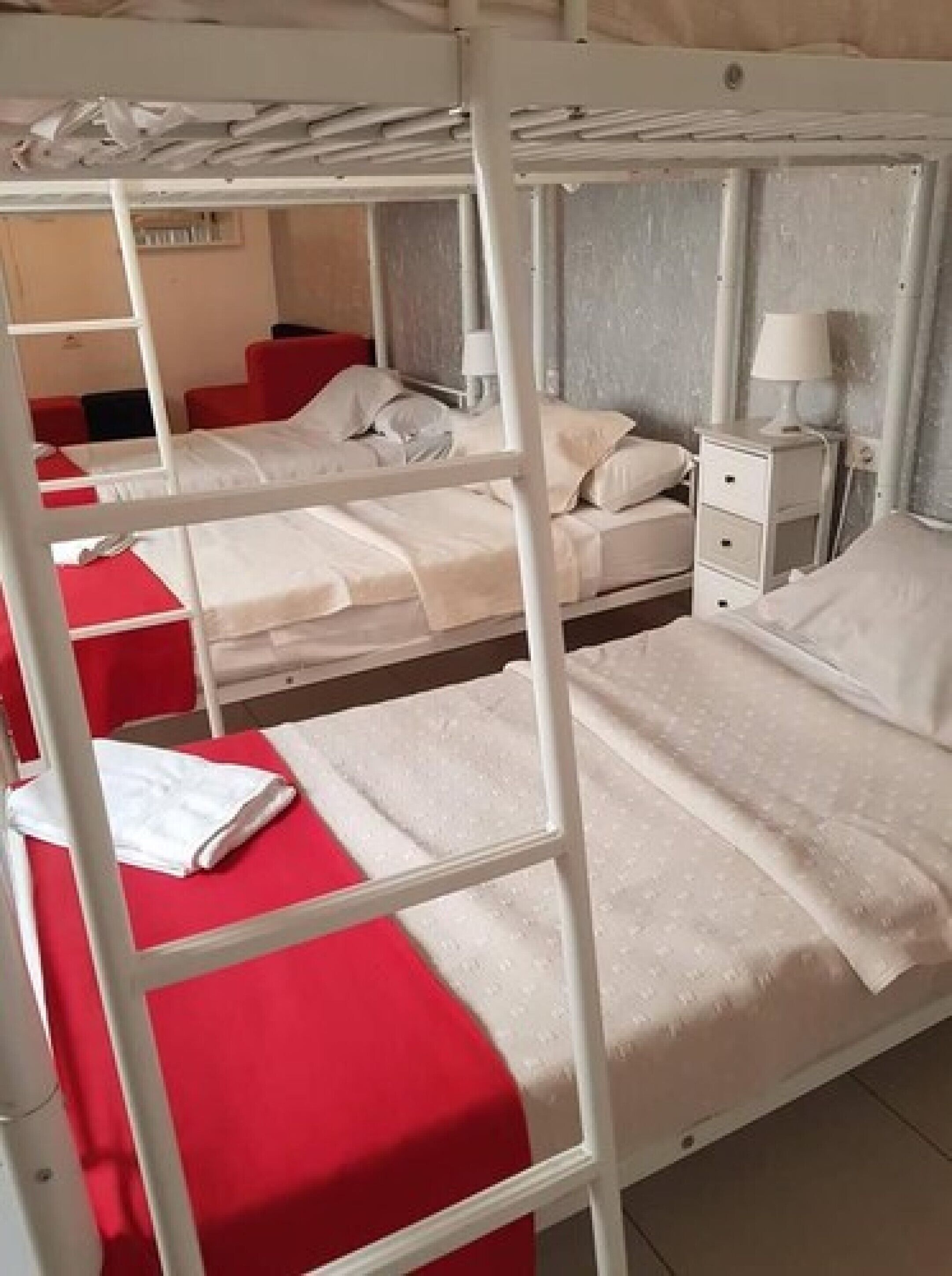 Een slaapkamer met een stapelbed, een rode sprei, wit beddengoed en een nachtkastje met een lamp.