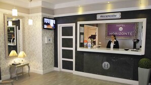 Een hotel receptie met een receptiebalie, een aan de muur bevestigde televisie en een bord met de tekst 'HOTEL HORIZONTE'.
