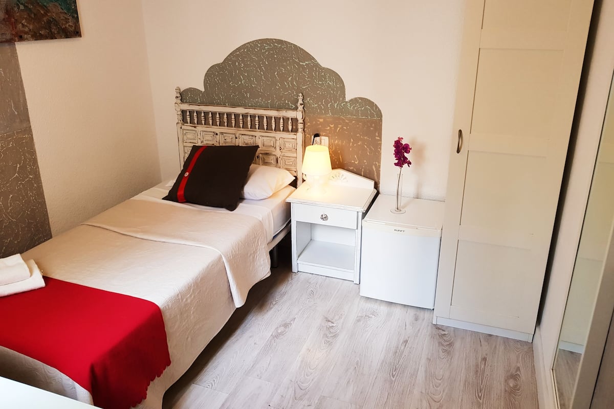 Une chambre à coucher comprenant un lit, une table de chevet avec une lampe, une petite table avec un vase et une armoire.