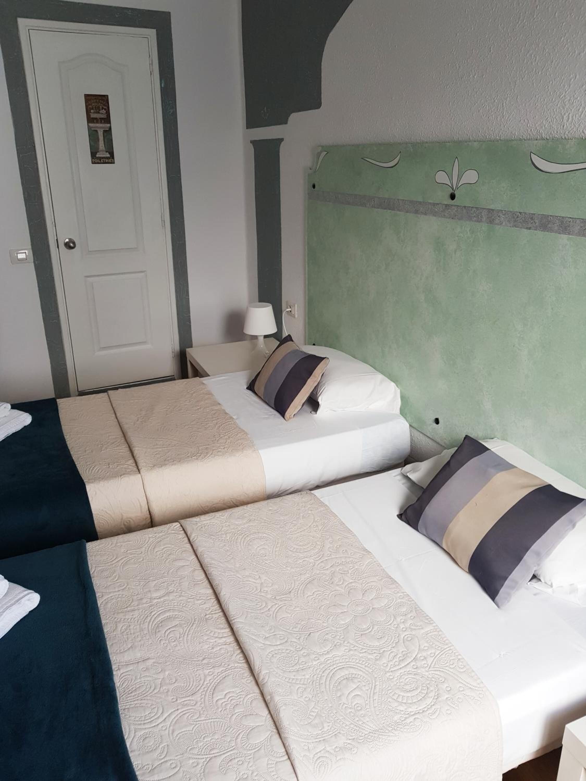 Habitación de hotel con dos camas, una puerta, una mesita de noche y una lámpara.