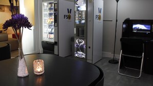 Een receptiegedeelte met een koffieapparaat, een vaas met paarse bloemen en een staande lamp.