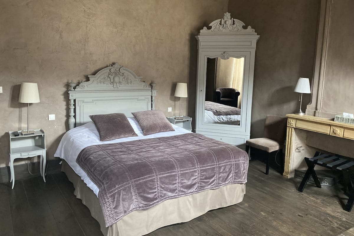 A bedroom with a bed, bedside tables, a mirror, a desk, and a chair.