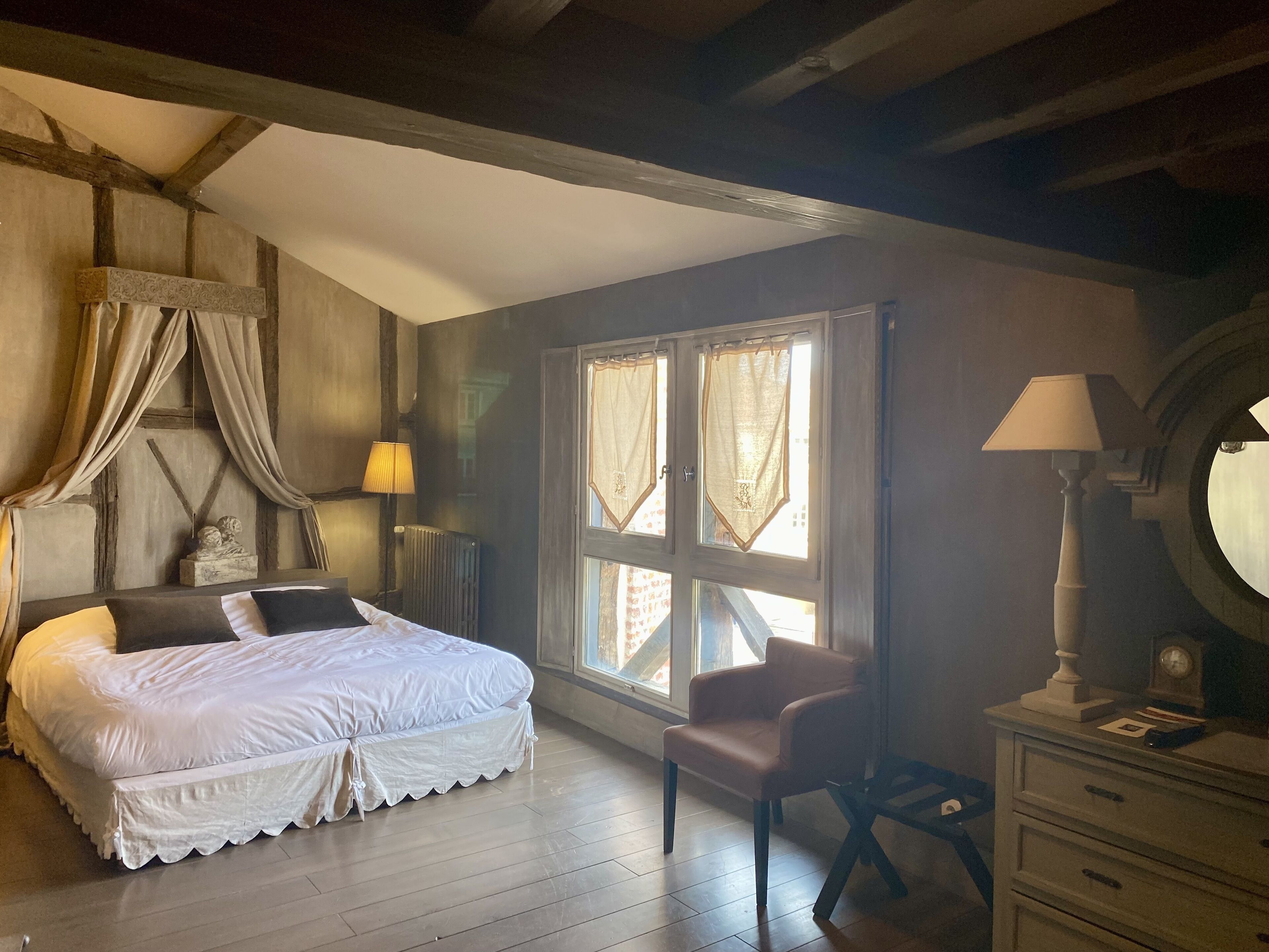 Une chambre à coucher avec un lit, une chaise, une commode et une fenêtre avec des rideaux.